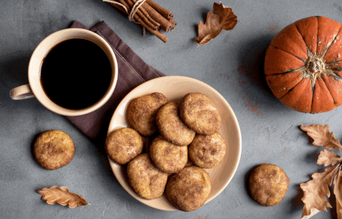 cup with coffee next to a plate of cookies, with fall leaves and a pumpkin