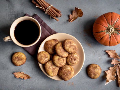 cup with coffee next to a plate of cookies, with fall leaves and a pumpkin