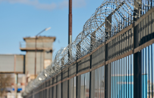 Fence with rolled barbed wire top, building in background