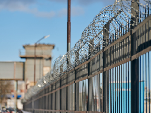 Fence with rolled barbed wire top, building in background