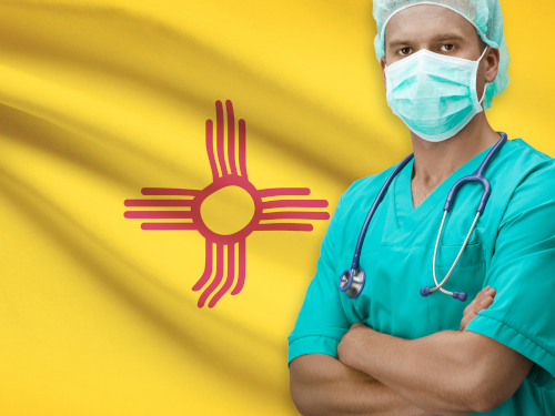 Doctor with stethoscope and surgical clothes in front of NM flag