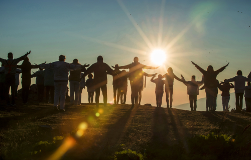 Silhouette of people on a hill at sunris raising hands to the sky