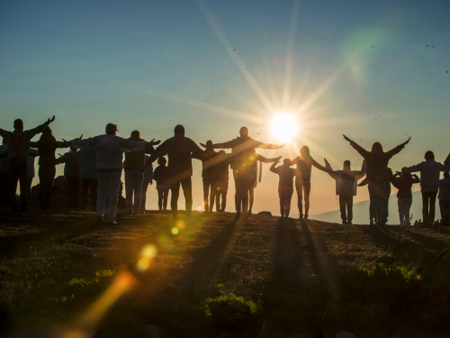 Silhouette of people on a hill at sunris raising hands to the sky