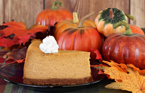 Slice of pumpkin pie sitting next to pumpkins and autumn leaves