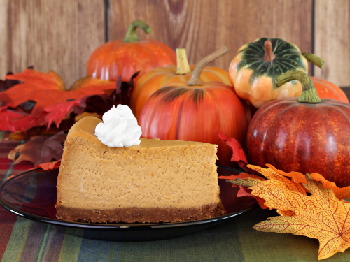 Slice of pumpkin pie sitting next to pumpkins and autumn leaves