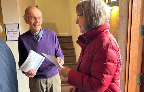 Usher handing a bulletin to woman in a red coat