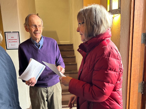 Usher handing a bulletin to woman in a red coat