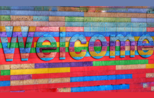 The word "Welcome" on a rainbow painted brick wall
