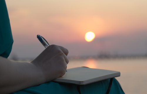 Woman writing in journal with sunset in background