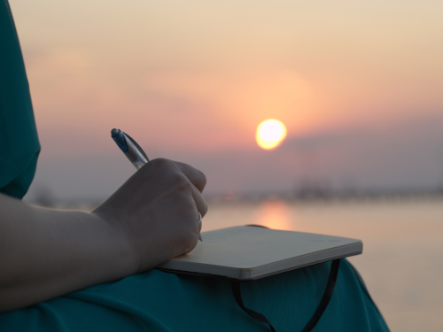 Woman writing in journal with sunset in background