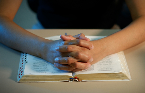 young hands folded on a bible