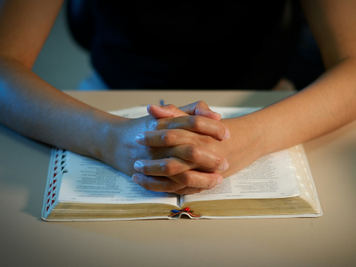 young hands folded on a bible
