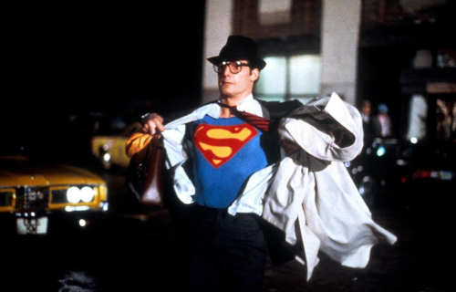 A still image from the Superman movie from the 1980s where Superman is taking off his shirt to reveal his Superman outfit underneath.