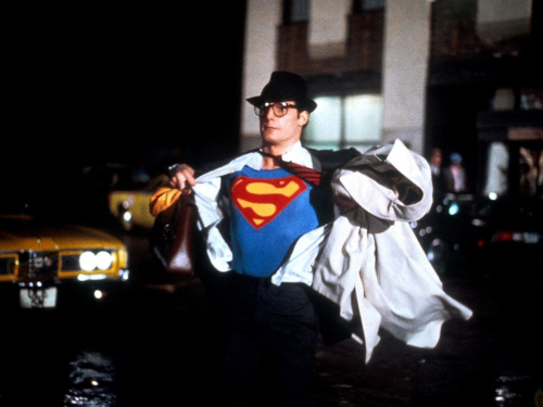 A still image from the Superman movie from the 1980s where Superman is taking off his shirt to reveal his Superman outfit underneath.